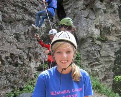 Teen girl wearing a helmet at a summer camp in Megève, participating in rock climbing activities.