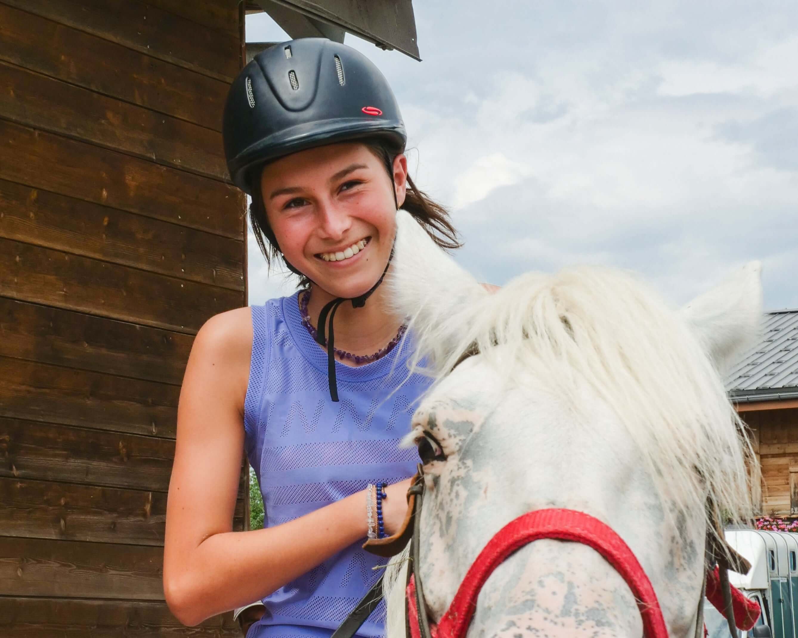 Teen girl smiling while riding a horse, wearing a helmet during a summer camp adventure.