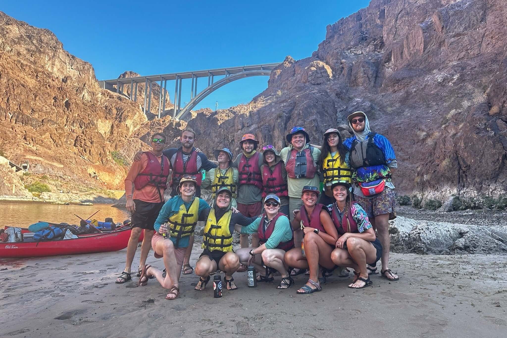 Group of adventure trip leaders and teens in life jackets by the river, ready for summer kayaking expedition.