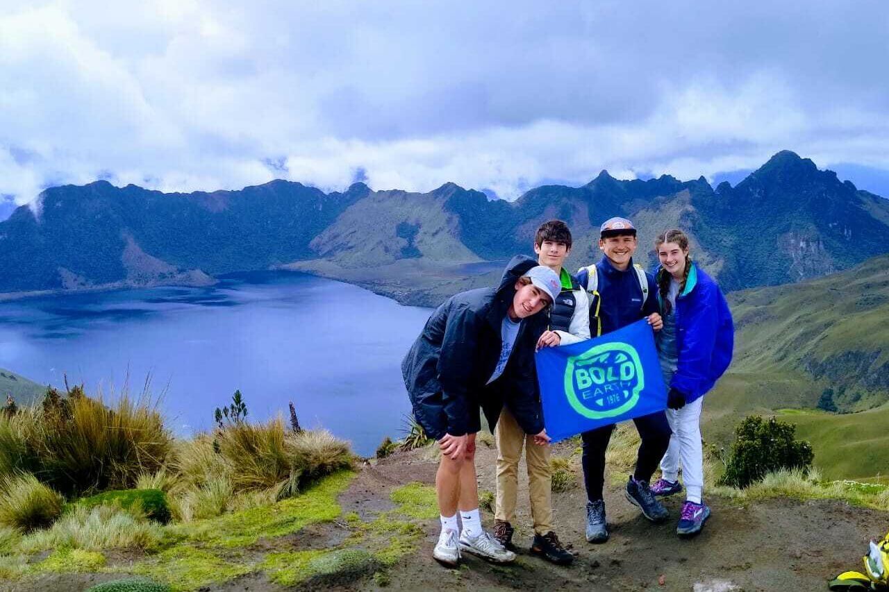 Teenagers on a mountain adventure holding a Bold Earth banner, promoting summer job and camp job experiences.