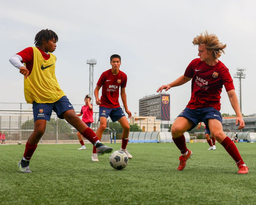 young soccer players training at a summer camp with FC Barcelona kits on a field.