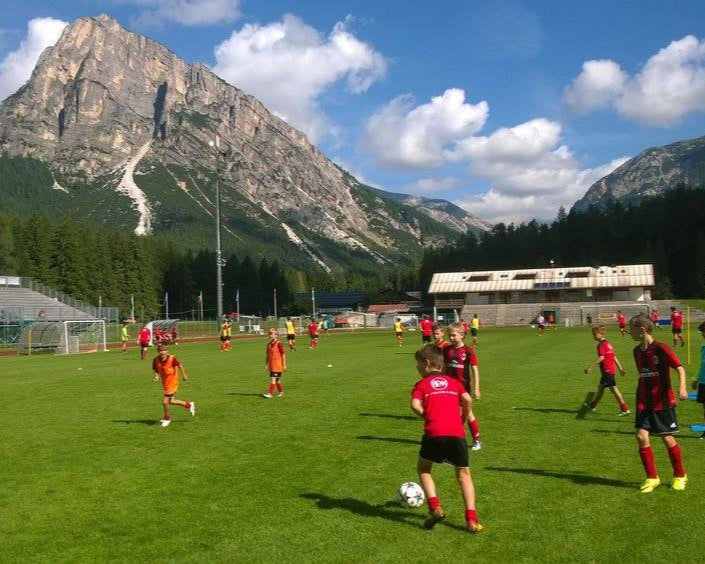 Young soccer players practicing on a green field with mountains in the background during summer camp training.