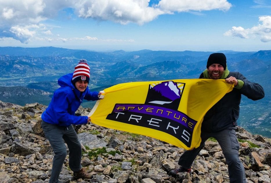 Two Adventure Treks participants proudly holding a flag atop a mountain in Colorado, celebrating their summer camp experience.