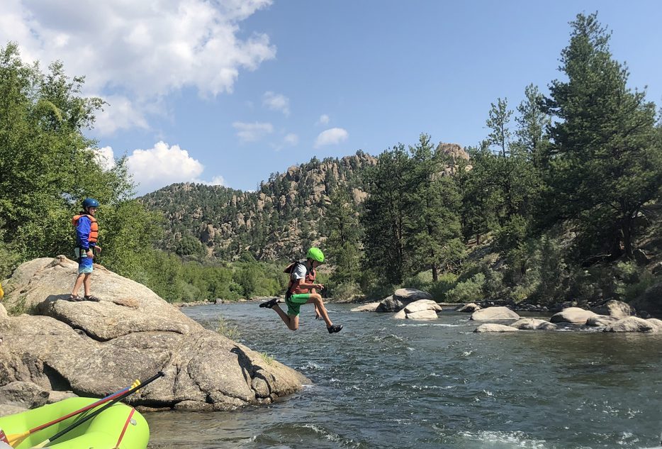 Kids enjoying summer adventure by jumping into a river in the Colorado wilderness during a travel camp experience.