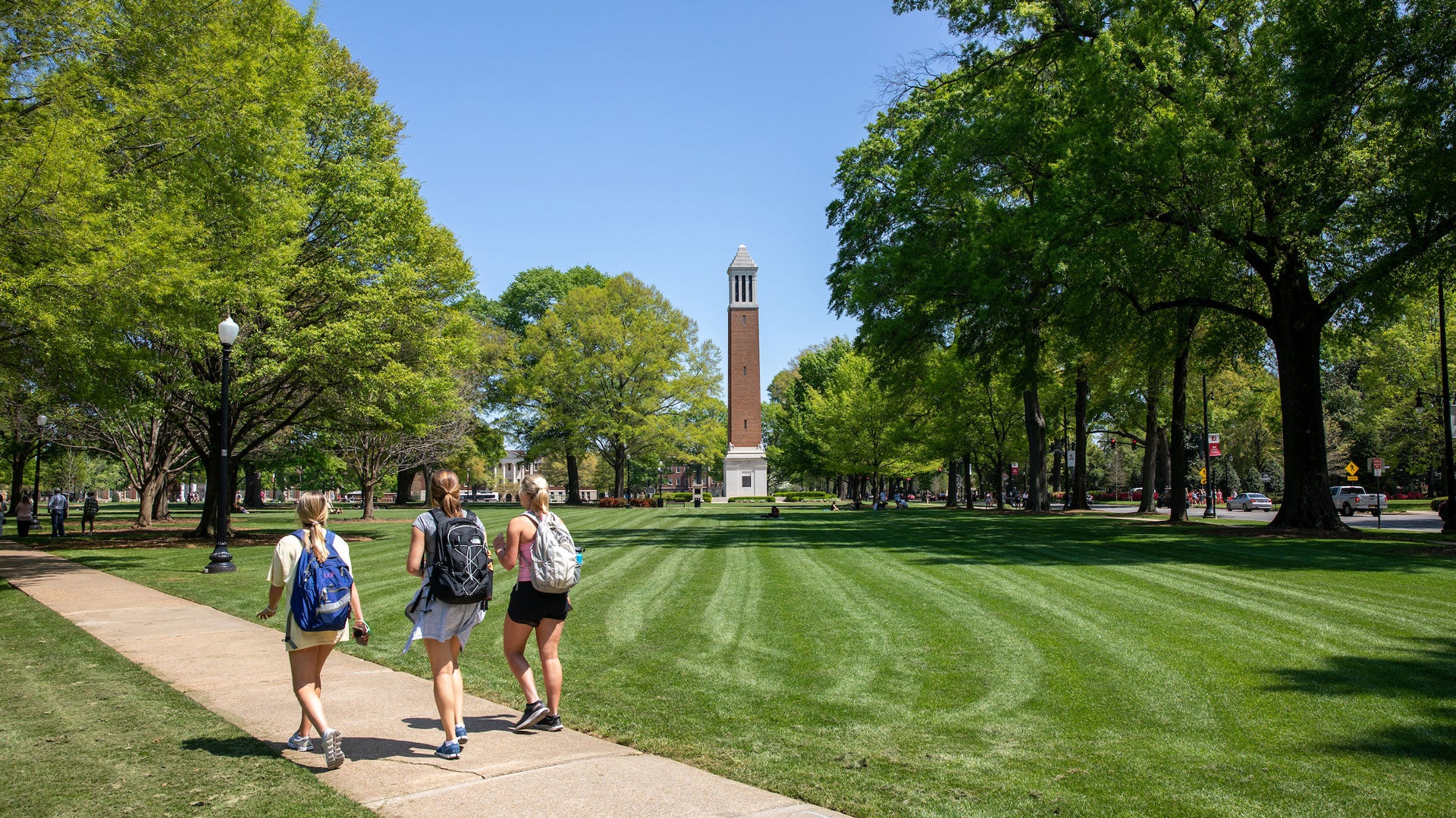 Students walking on a college campus during a sunny day, highlighting summer programs and outdoor activities.