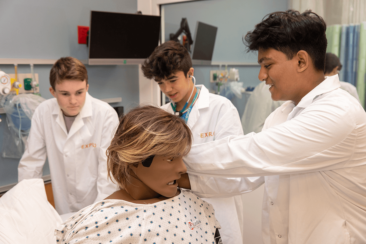 middle school students participating in a summer program, learning medical skills with a mannequin in a lab setting.