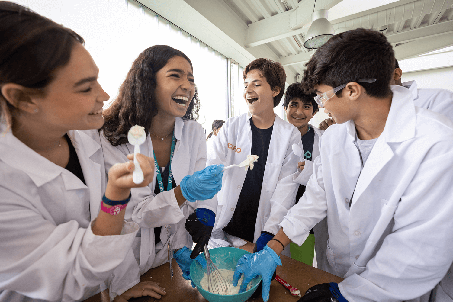 Middle school students participating in a fun science experiment while wearing lab coats, laughing and mixing ingredients.