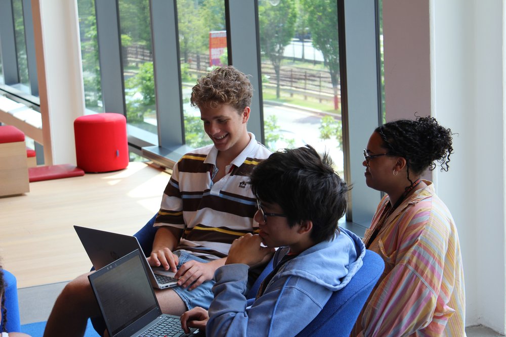 High school students collaborating on laptops in a modern learning space, enhancing skills for success in summer programs.