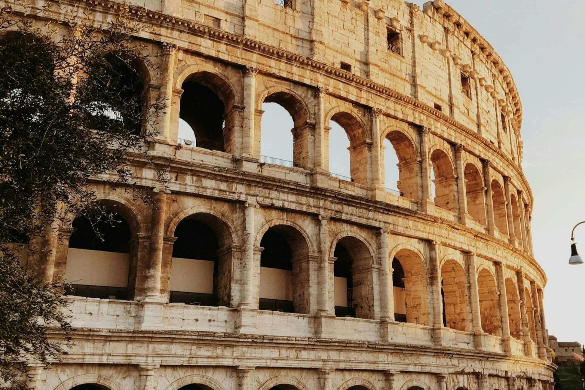 Ancient Roman Colosseum exterior view, showcasing its iconic arches and historical architecture at sunset.