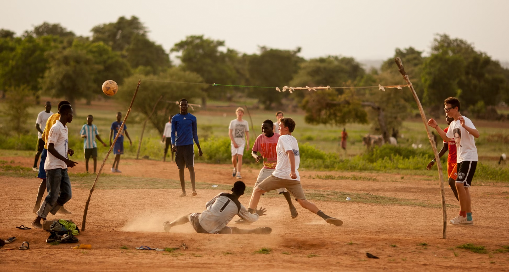 Group of children playing soccer on a dirt field, showcasing teamwork and enjoyment in a summer outdoor setting.