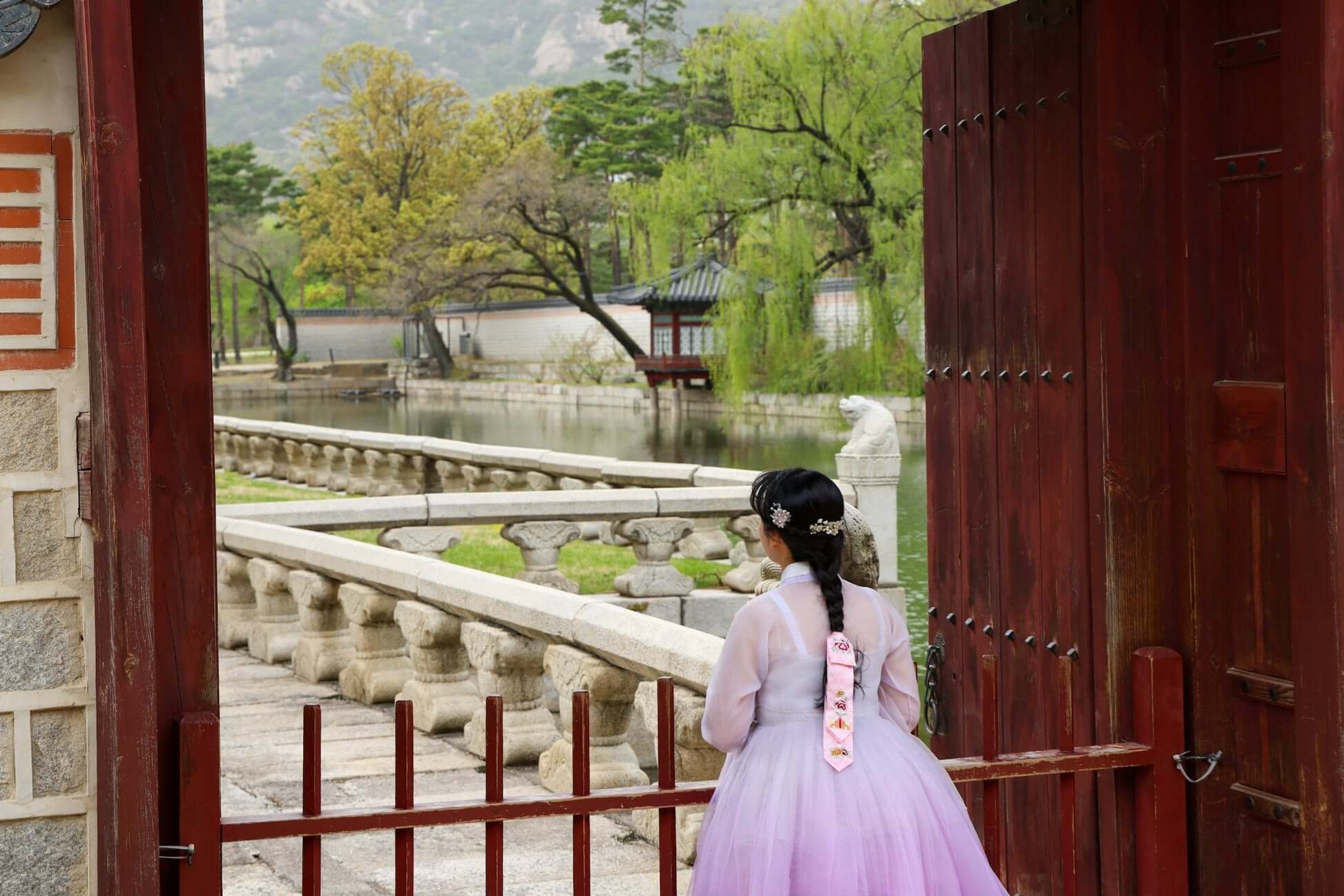 Teen girl in a hanbok overlooking a serene lake and traditional Korean architecture, capturing South Korea's beauty.