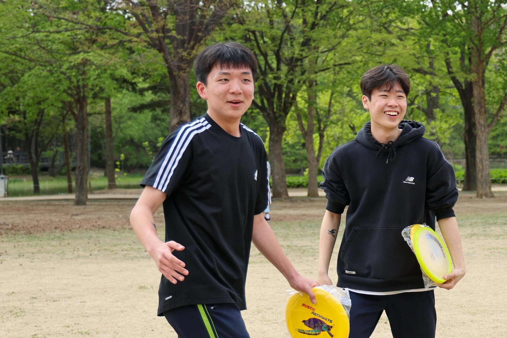 Two teens enjoying a sunny day outdoors, playing with frisbees in a park in South Korea.