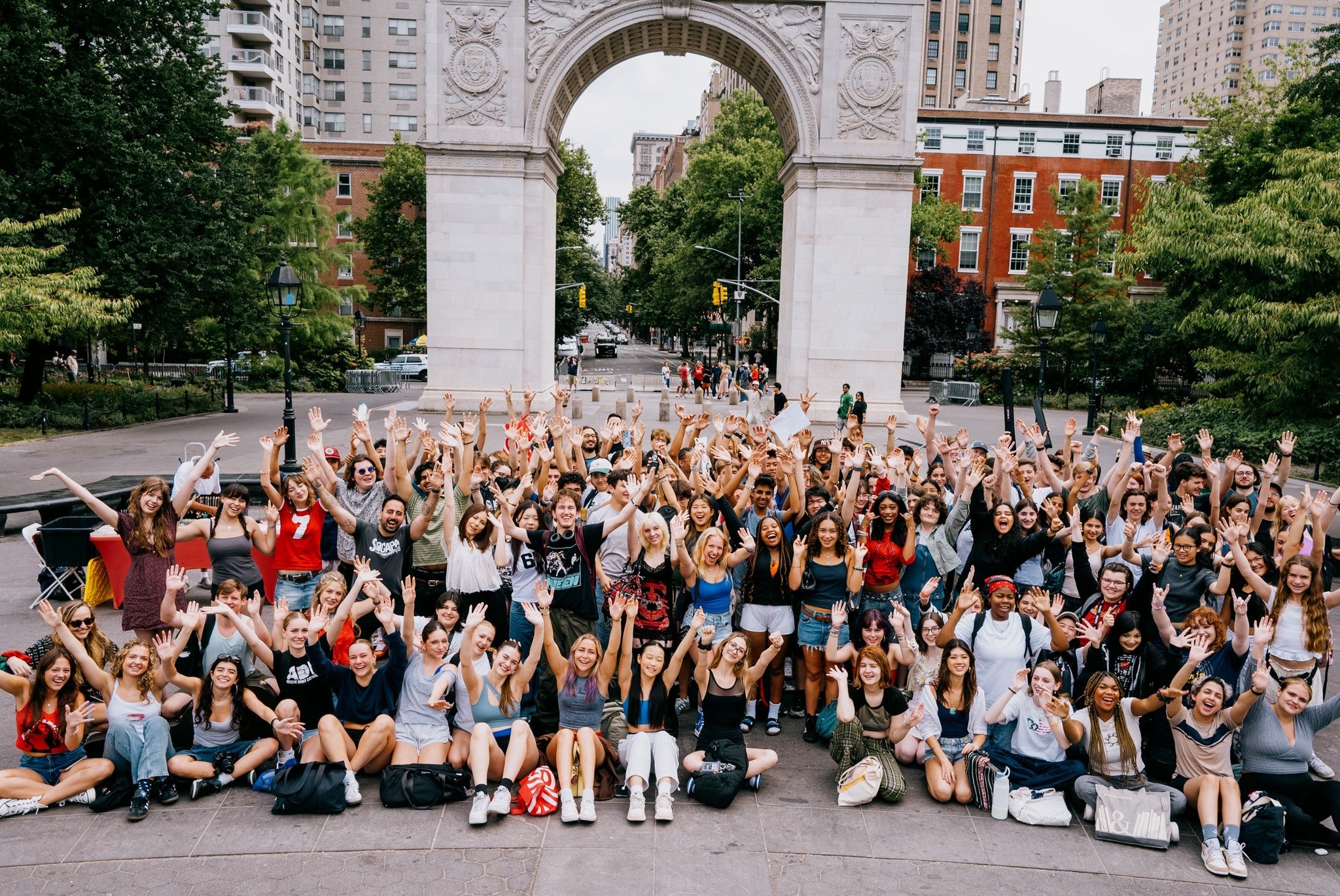 Diverse group of high school students joyfully gathered under an arch in a city park, celebrating summer programs and activities.