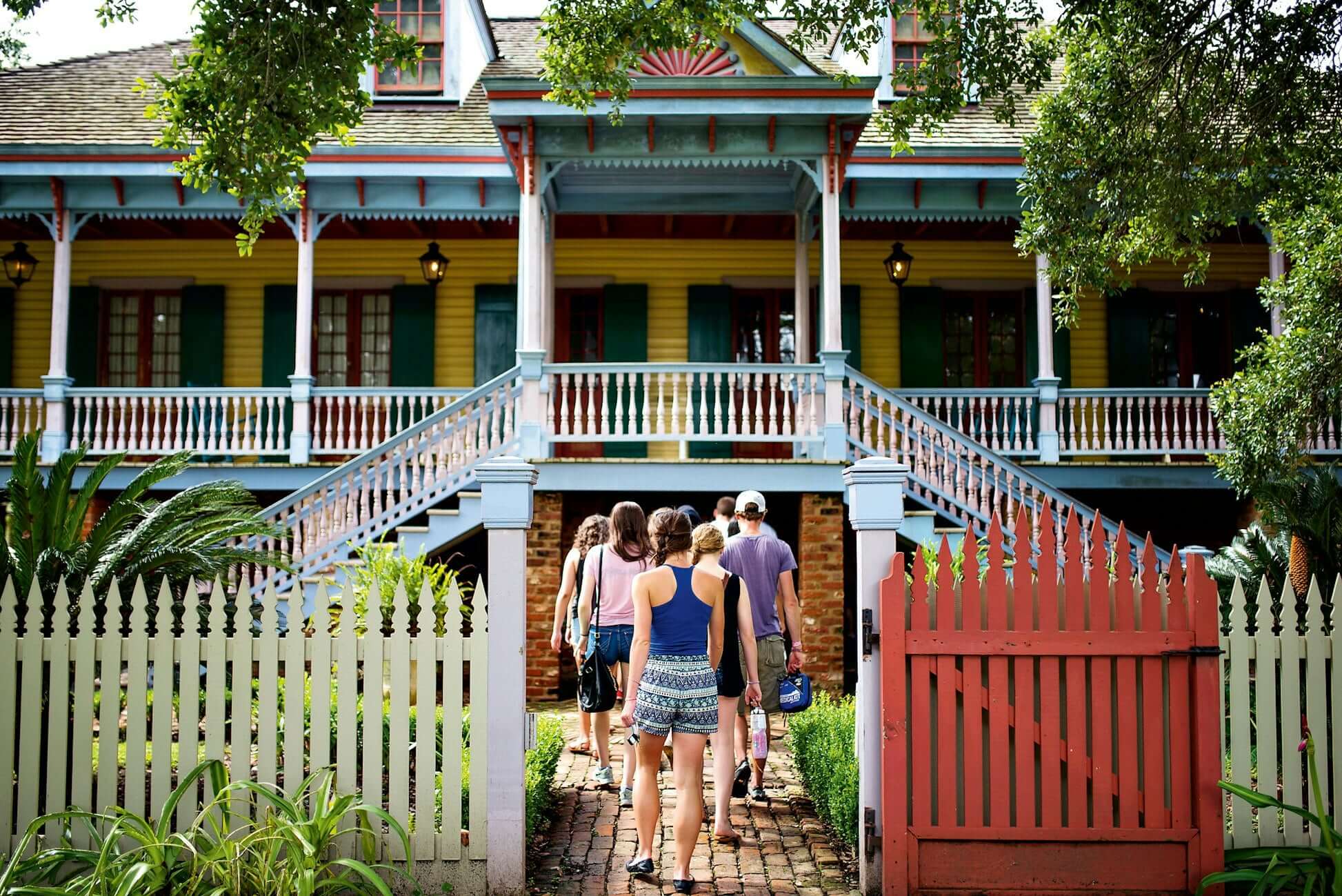 Participants in a high school summer program walk towards a colorful New Orleans house surrounded by greenery.