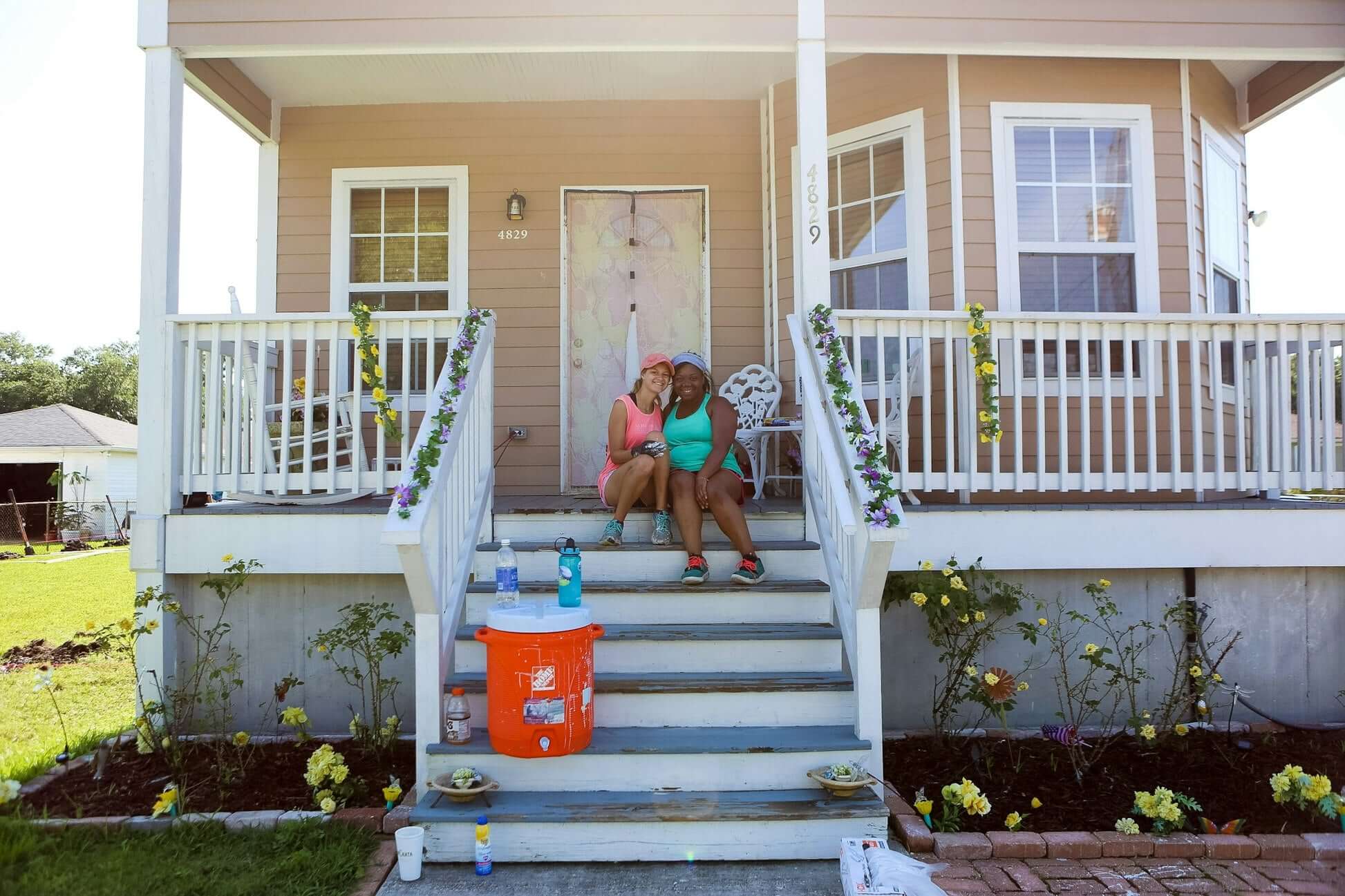 Two women sitting on the steps of a newly renovated home in New Orleans, embodying community rebuilding efforts.