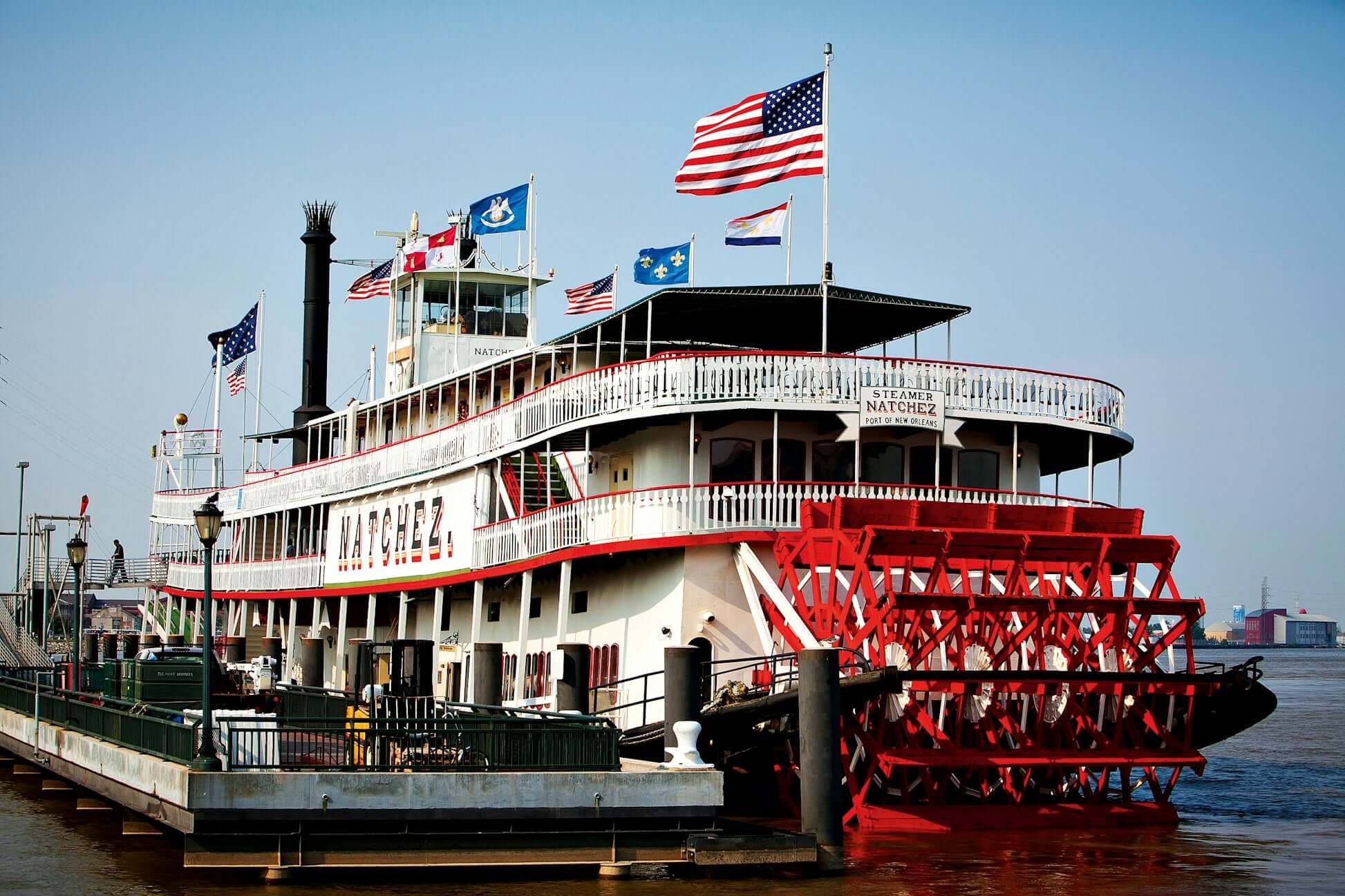 Steamboat Natchez docked on the Mississippi River, showcasing American flags and classic paddlewheel design.