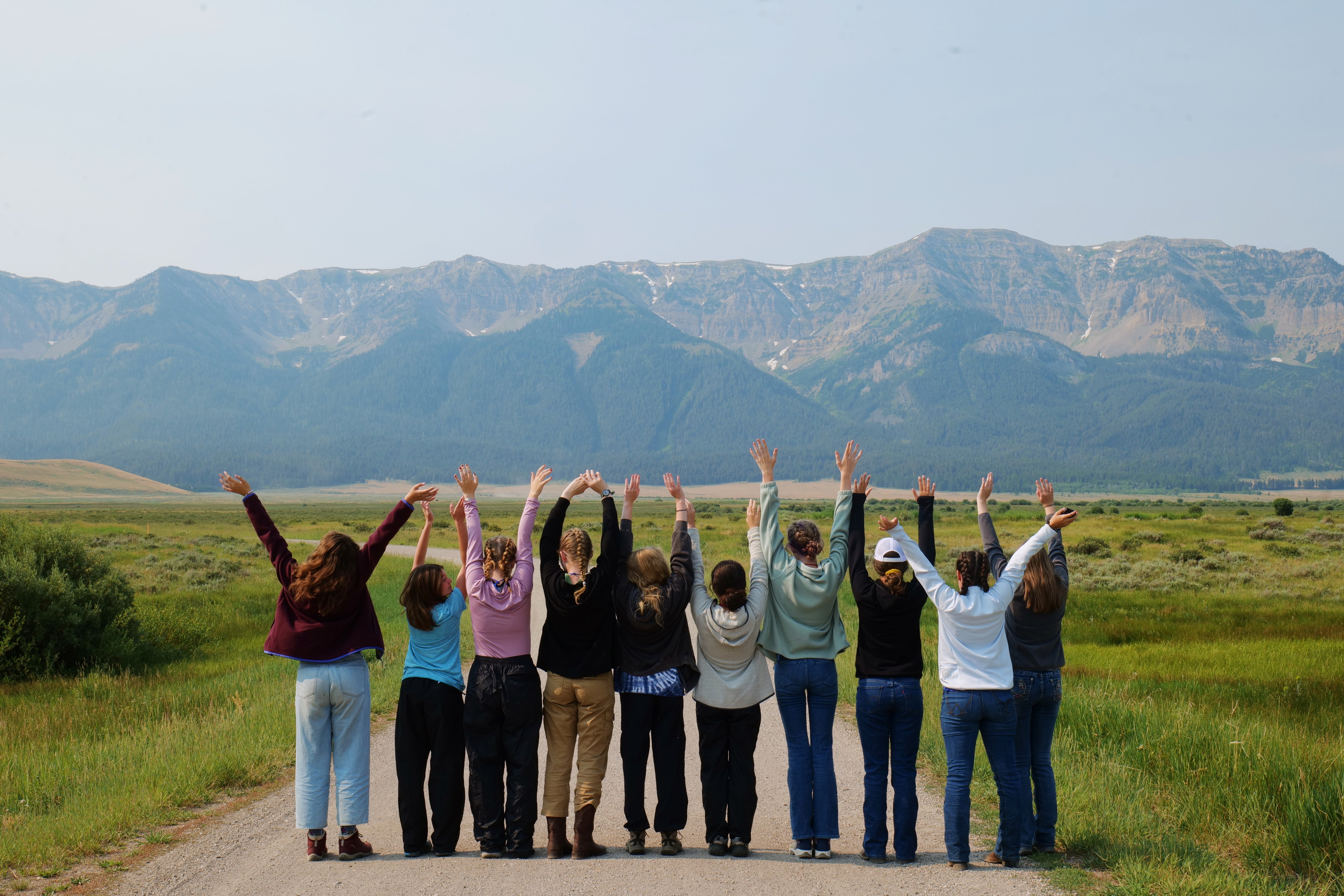 Group of campers joyfully raising hands in the mountains during Alpengirl summer adventure camp.