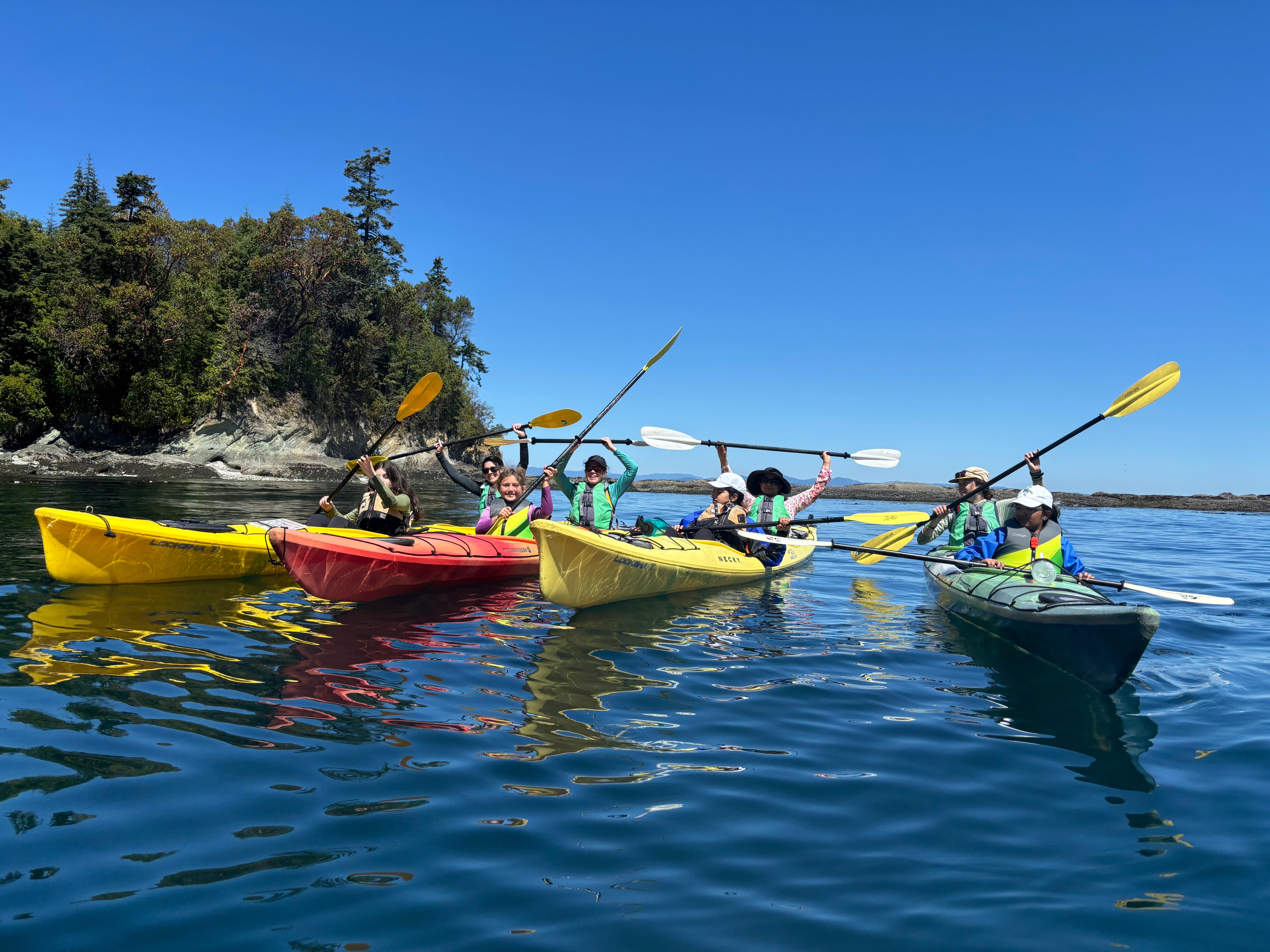 Teen campers enjoying a summer kayak adventure in colorful boats on a sunny day at Alpengirl Camp.