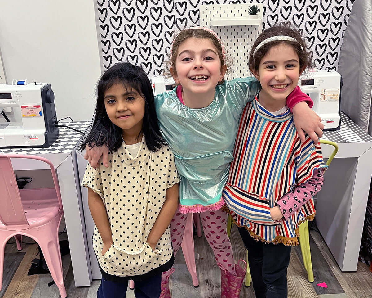 Kids enjoy the Fashion Design Summer Camp in NYC, showcasing their handmade clothing creations and smiling together.