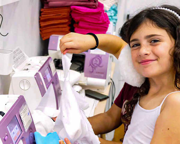 Young girl sewing at a Fashion Design Summer Camp for Kids in New York City, smiling and engaging in creative projects.