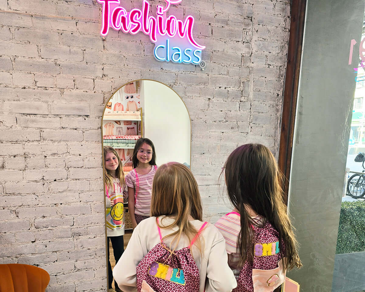 Kids at Fashion Design Summer Camp in NYC admire themselves in a mirror, showcasing creativity and fun.