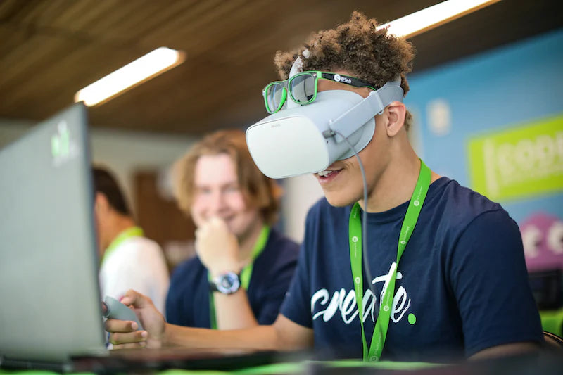 Teen using virtual reality headset at summer program, focused on creating digital content with peers in the background.